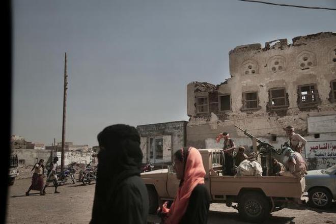 In this Feb. 12, 2018, photo, women walk past Saudi-led coalition backed forces, leading the campaign to take over Hodeida, as they patrol Mocha, a port city on the Red Sea coast of Yemen.