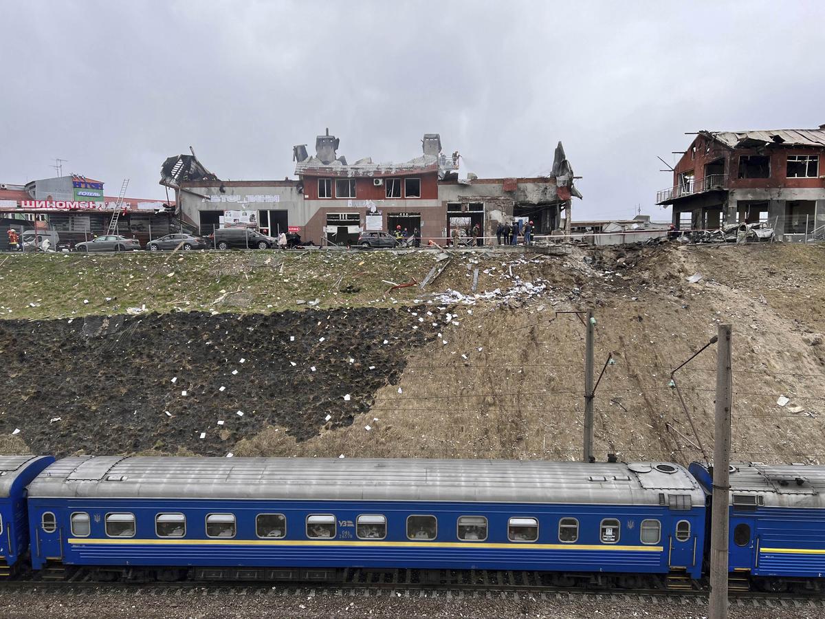 A train travelling from Dnipro passes by the area where emergency workers clear up debris after an airstrike hit a tire shop in the western city of Lviv, Ukraine on April 18, 2022. 