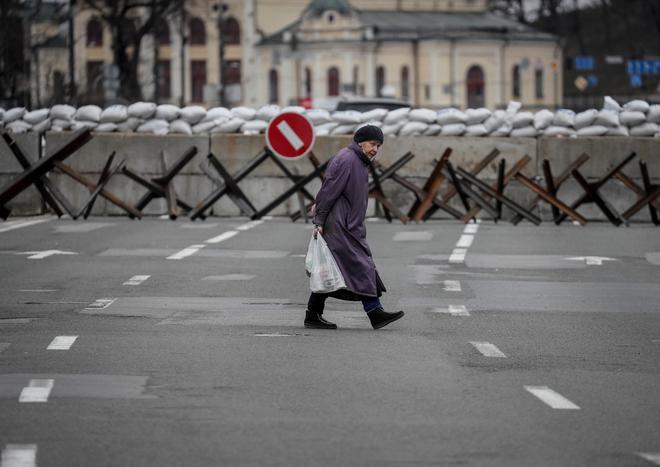 7 मार्च, 2022 को मध्य कीव, यूक्रेन में टैंक-विरोधी निर्माण दिखाई देने पर एक महिला सड़क पार करती है।