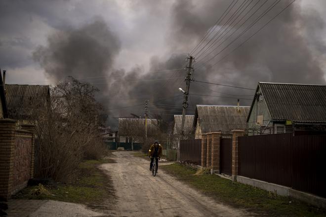 A Ukrainian man rides his bicycle near a factory and a store burning after it had been bombarded in Irpin, on the outskirts of Kyiv, Ukraine, on March 6, 2022. 