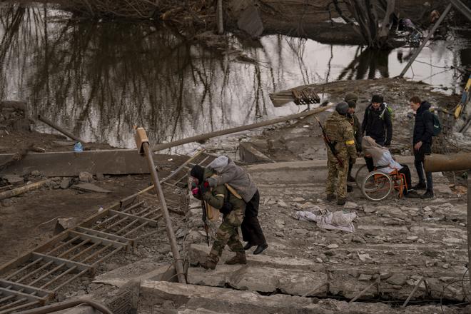 A Ukrainian soldier carries an elderly woman crossing the Irpin river on the outskirts of Kyiv, Ukraine, Monday, March 7, 2022.