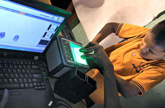 Aadhaar centre computer operator assists young boy in placing his thumbs firmly on biometric sensor machine.