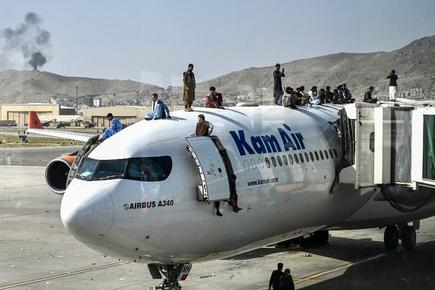 Afghan people climb atop a plane as they wait at the airport in Kabul on August 16, 2021.